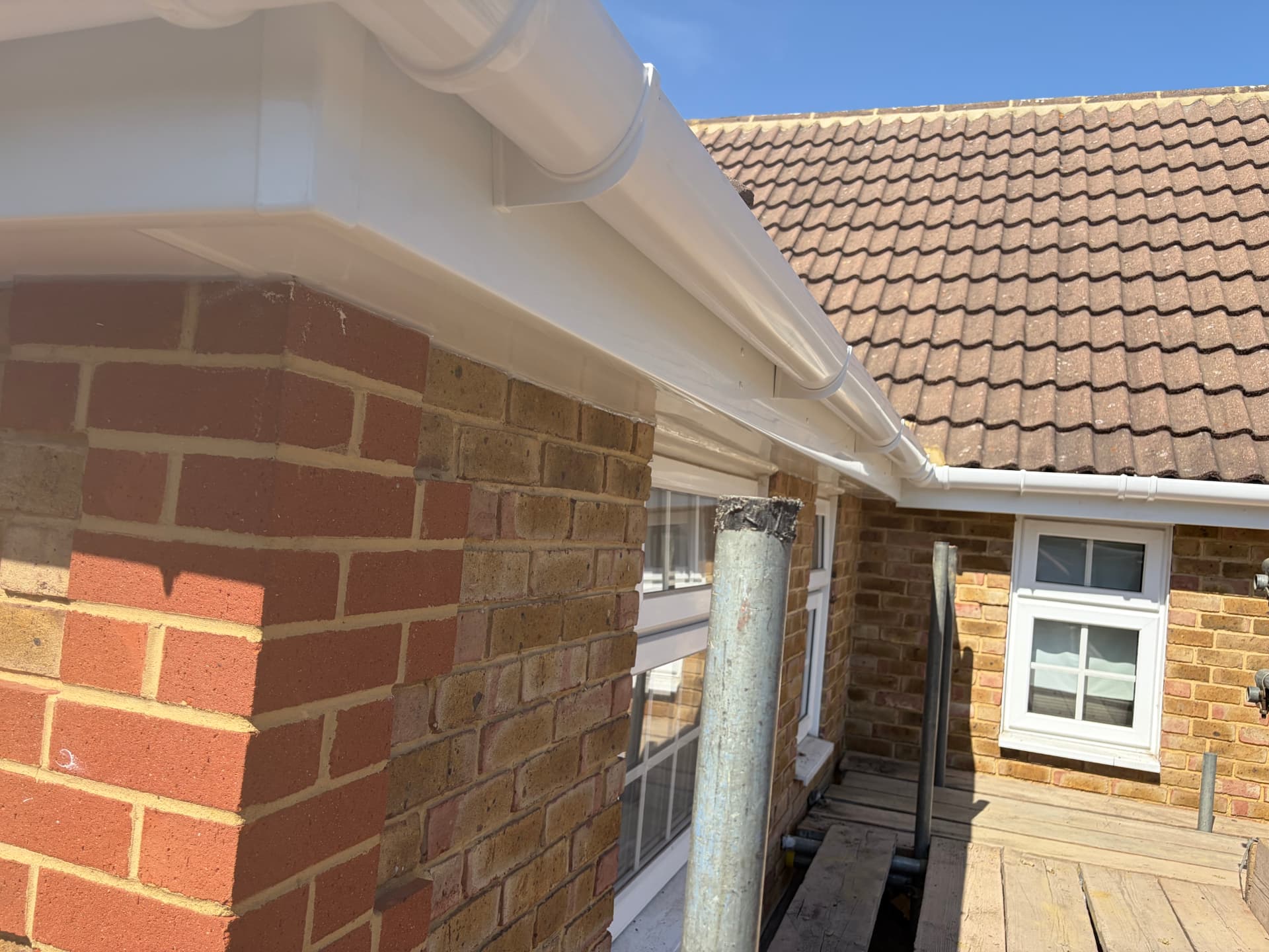 Perspective view of new white fascia and guttering running along the brick wall with scaffold in place