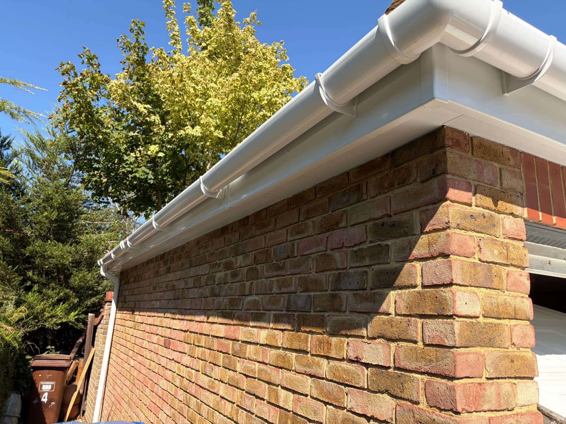 Completed white guttering and soffit running along the brick wall in sunshine after scaffold strike