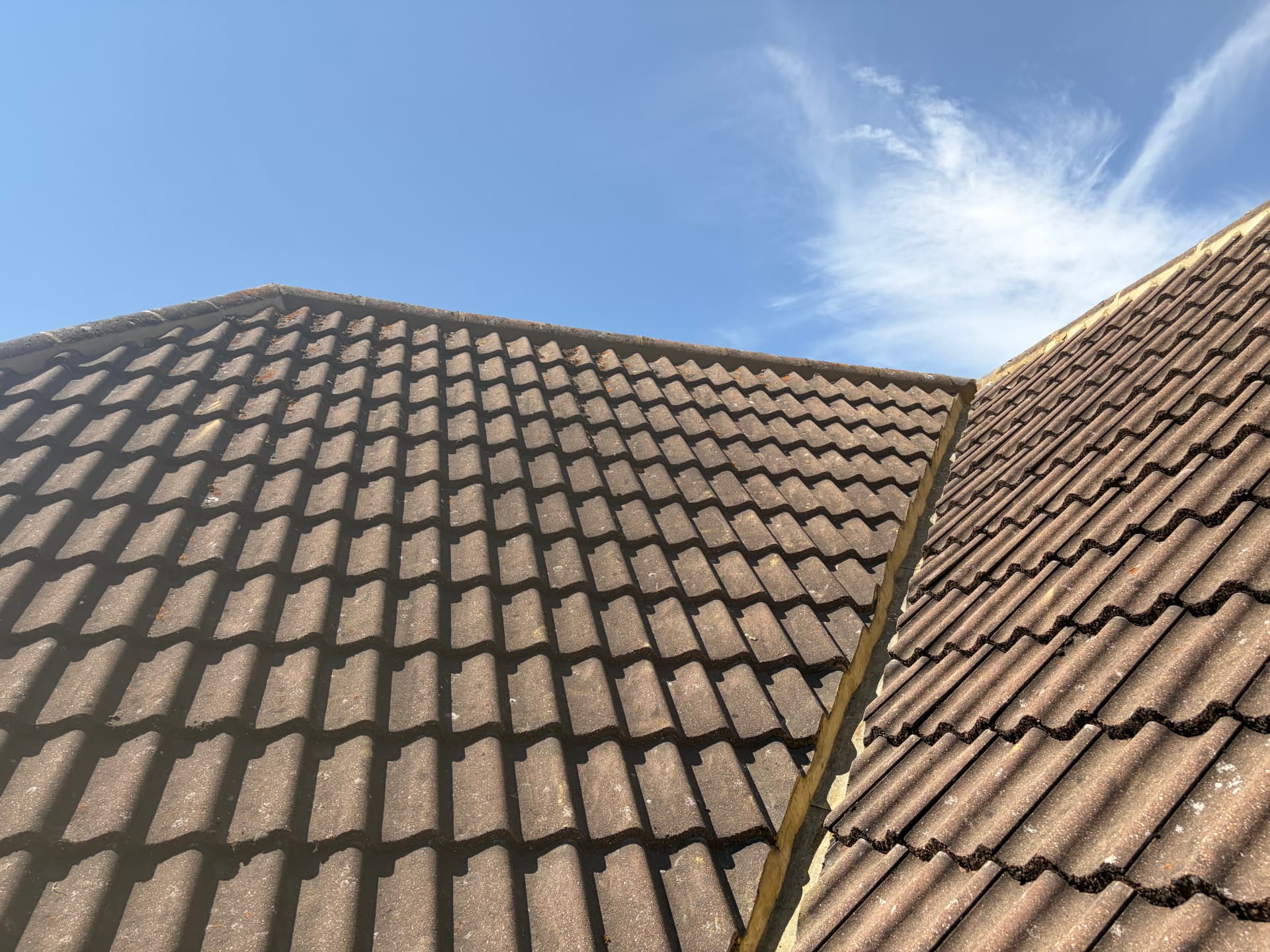 Rebedded hip and ridge mortar between two tiled roof slopes against a clear blue sky