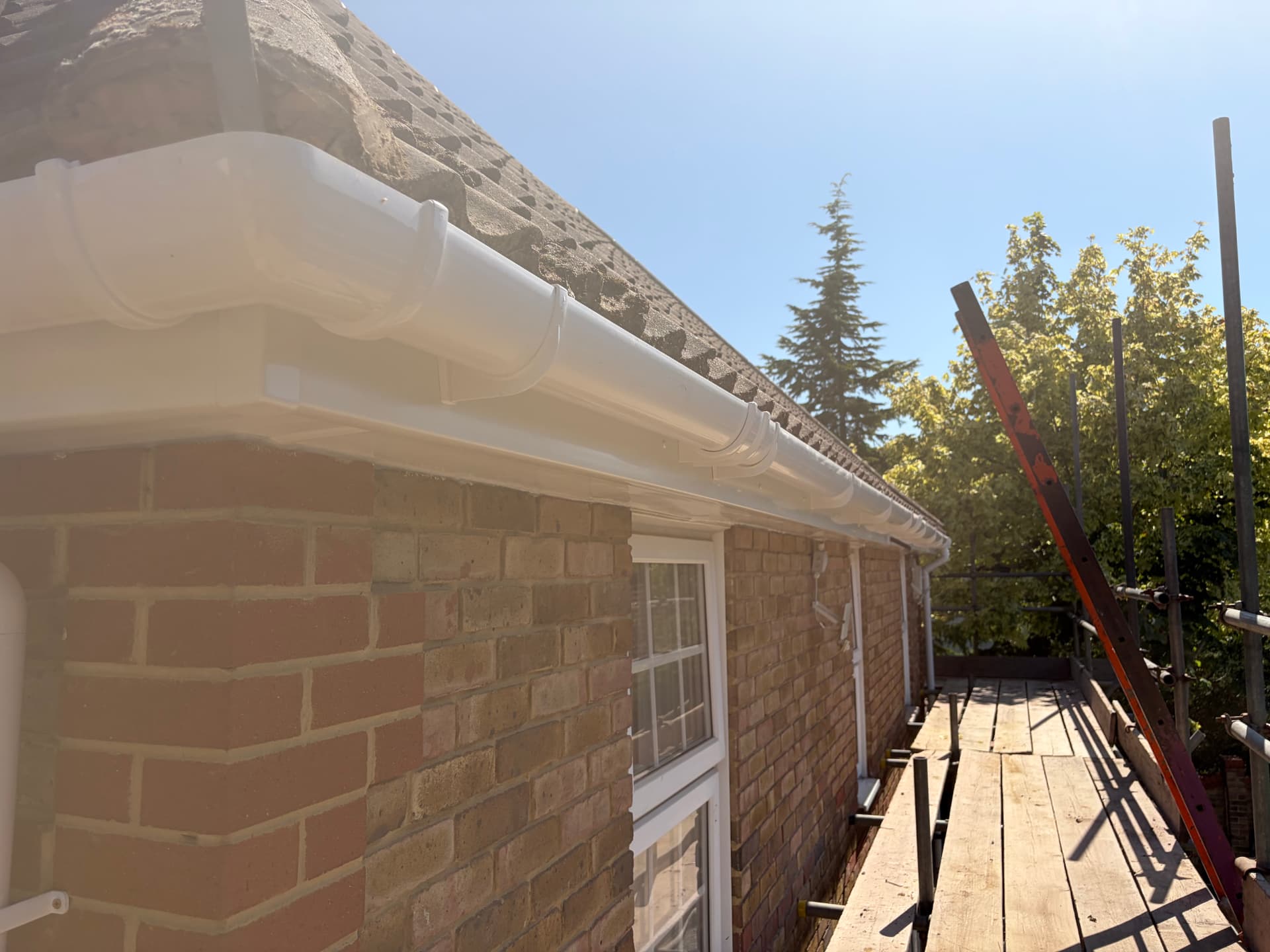 Close-up of new white uPVC guttering, fascia and soffit installed along the brick wall