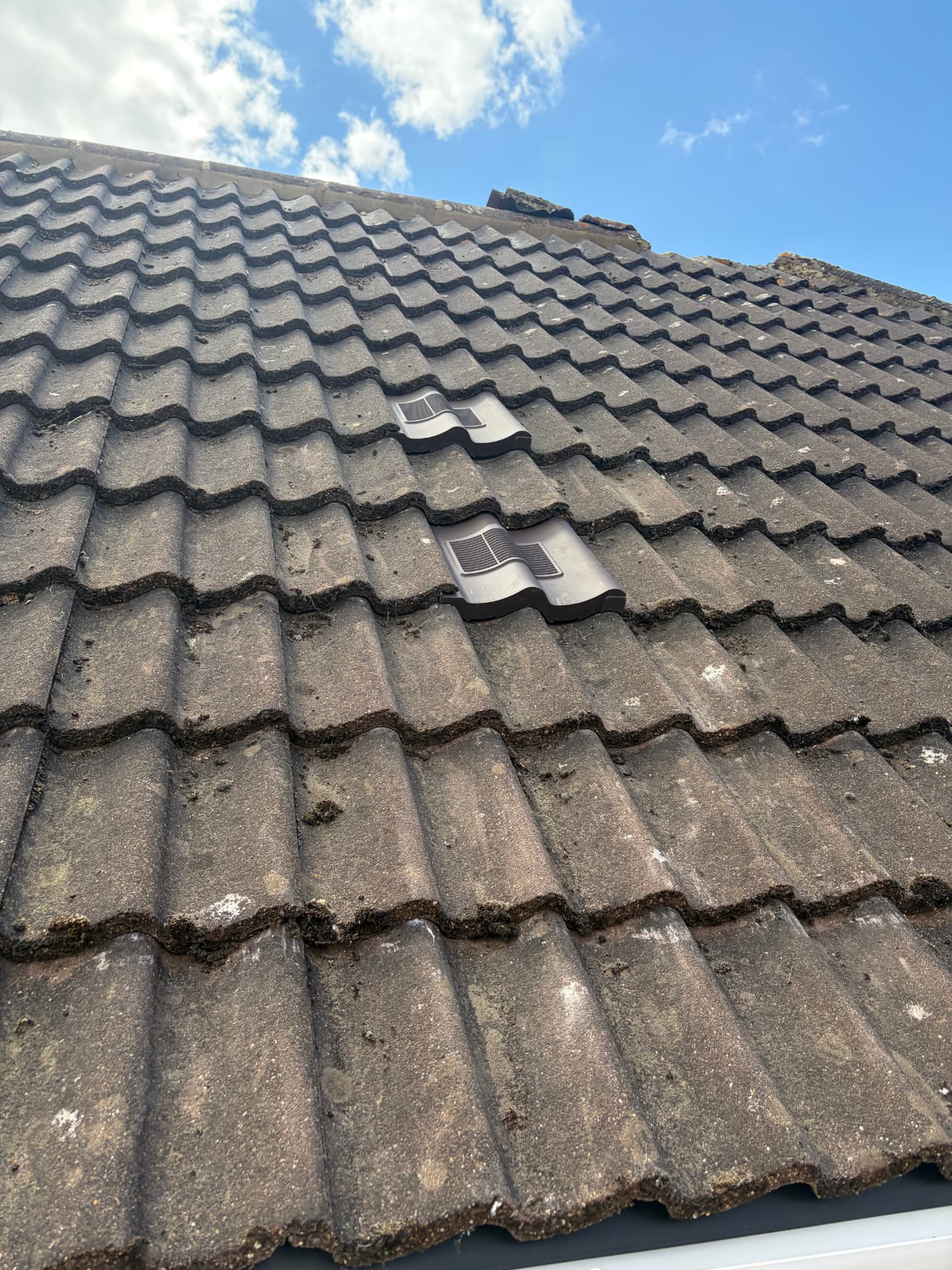 Close-up of weathered tiles with two newly fitted dark grey tile vents serving the bathroom extracts