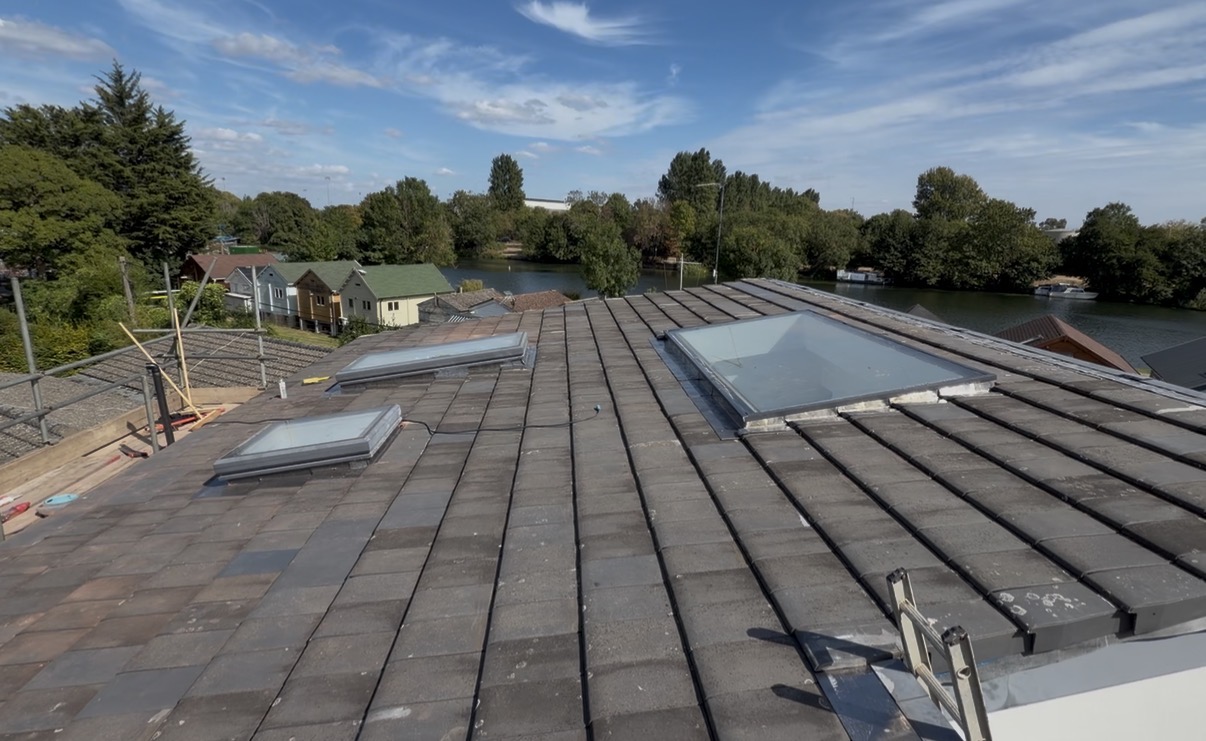 Re-tiled riverside roof in Sunbury-on-Thames nearing completion, with three rooflights fitted and the river visible beyond