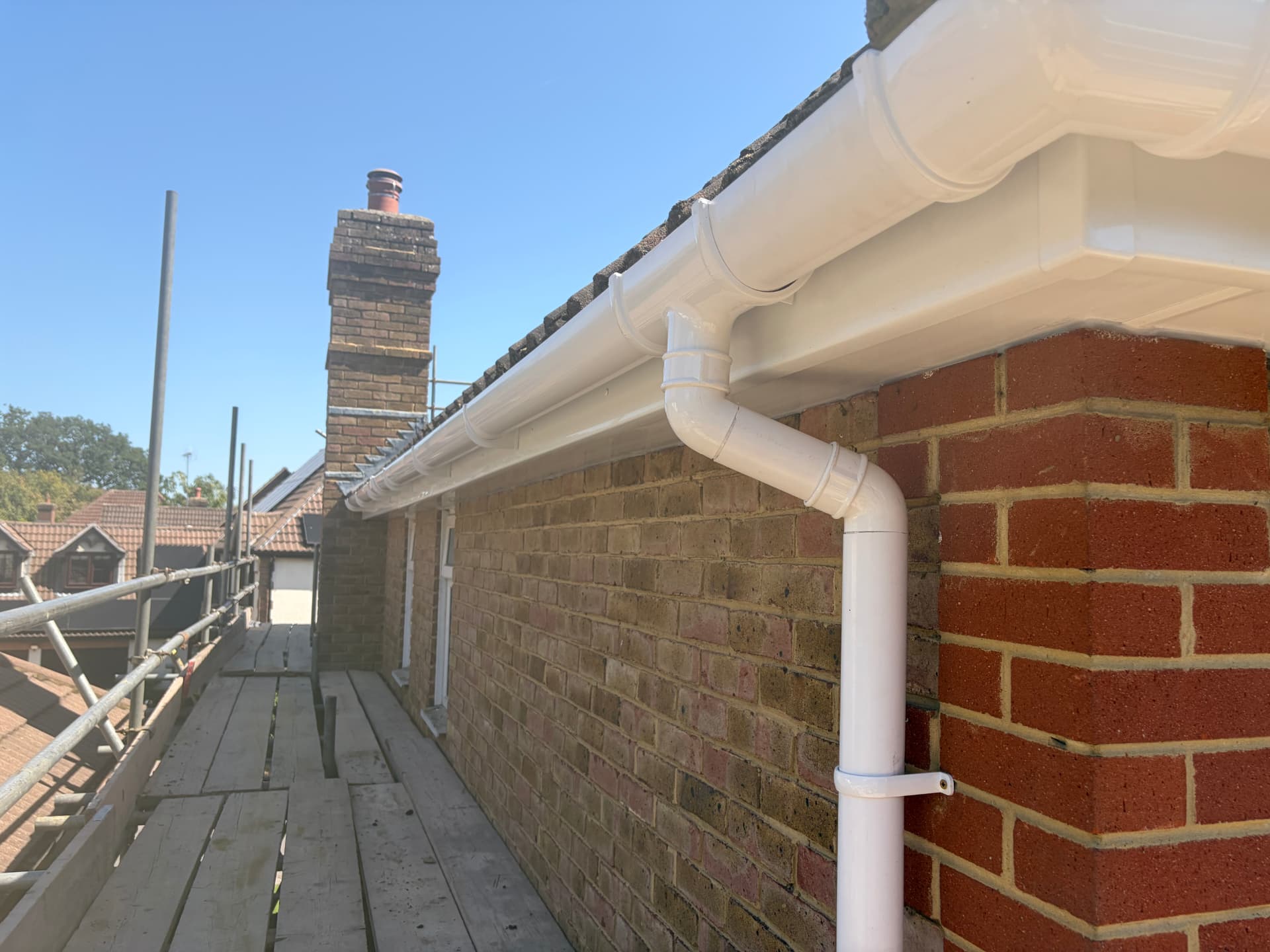 New white uPVC downpipe joined to the guttering with fresh fascia and soffit above